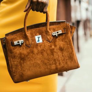Chic brown leather handbag held by a fashionable woman in a vibrant cityscape.